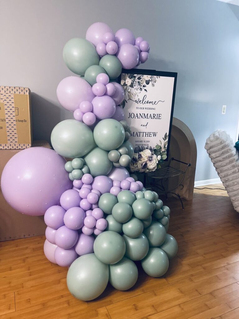 Sage green and lavender organic balloon garland framing a floral wedding welcome sign