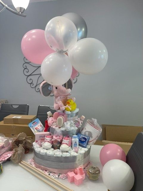 Tiered diaper cake gift topped with a plush elephant and a pink balloon bouquet