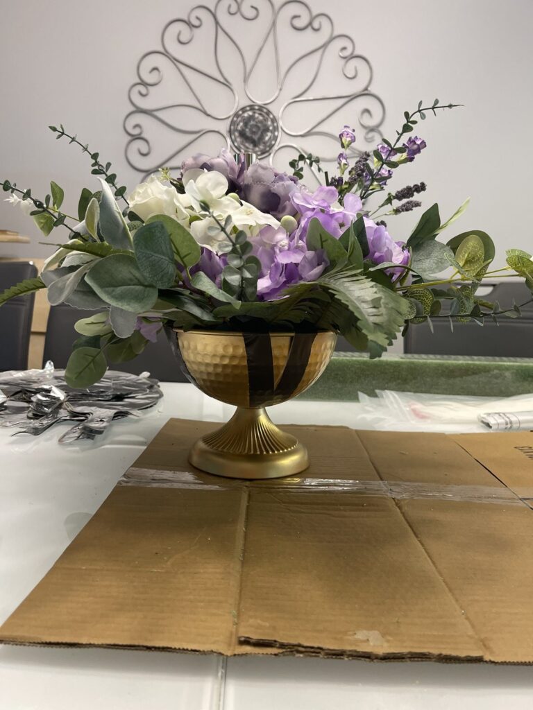 Purple and white floral centerpiece in a gold pedestal urn