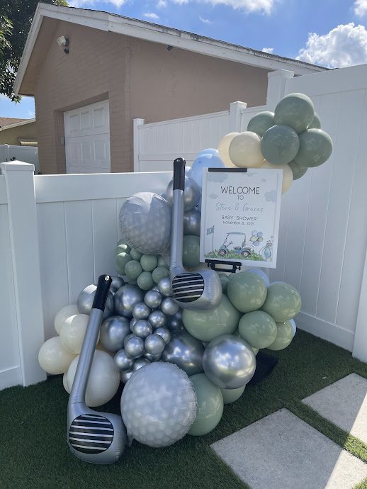 Sage green and chrome balloon display with oversized golf club balloons beside a baby shower welcome sign