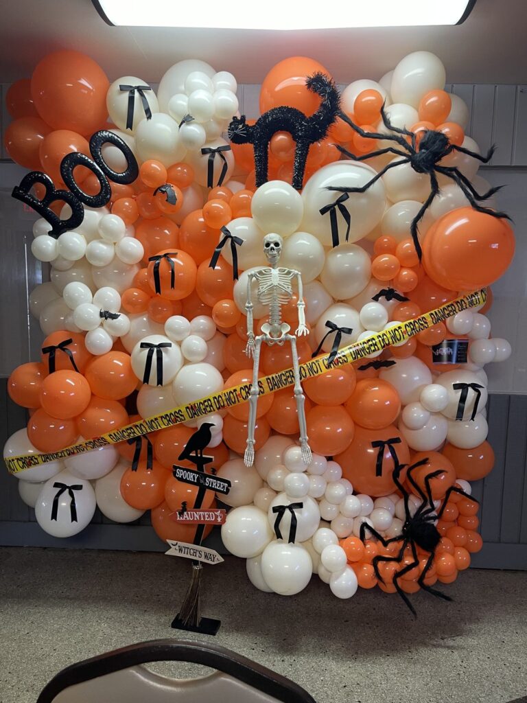 Orange, black and white Halloween balloon wall with spiders, a skeleton and BOO lettering
