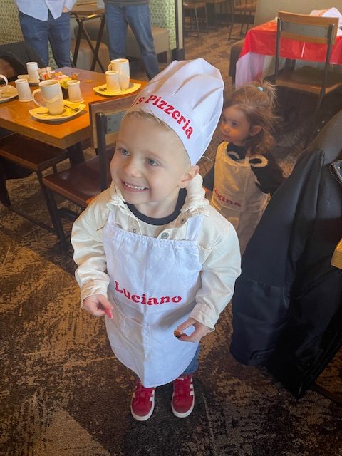 Young guest in a chef hat and apron at a hosted pizzeria party experience