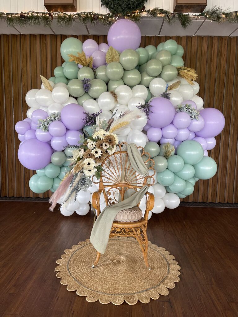 Lavender, mint and white balloon installation surrounding a rattan peacock chair with dried florals