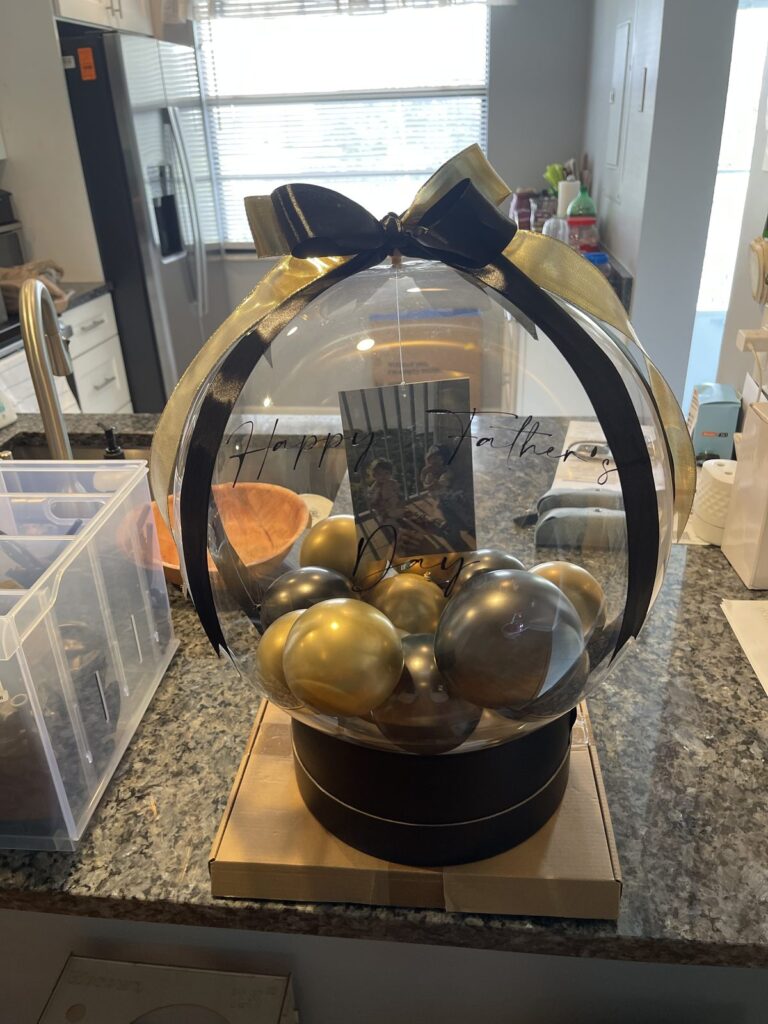 Black and gold stuffed balloon gift box with a black satin bow