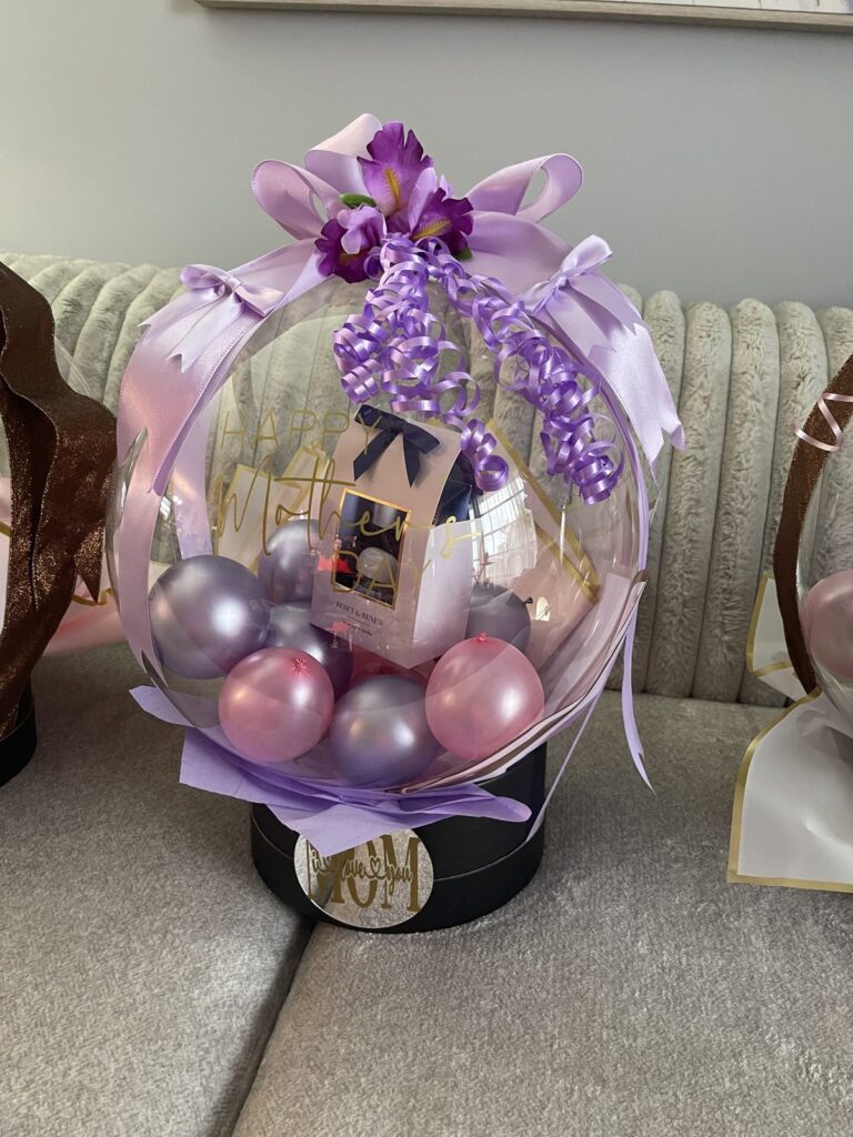 Clear stuffed balloon gift filled with lavender and pink balloons and topped with a purple bow